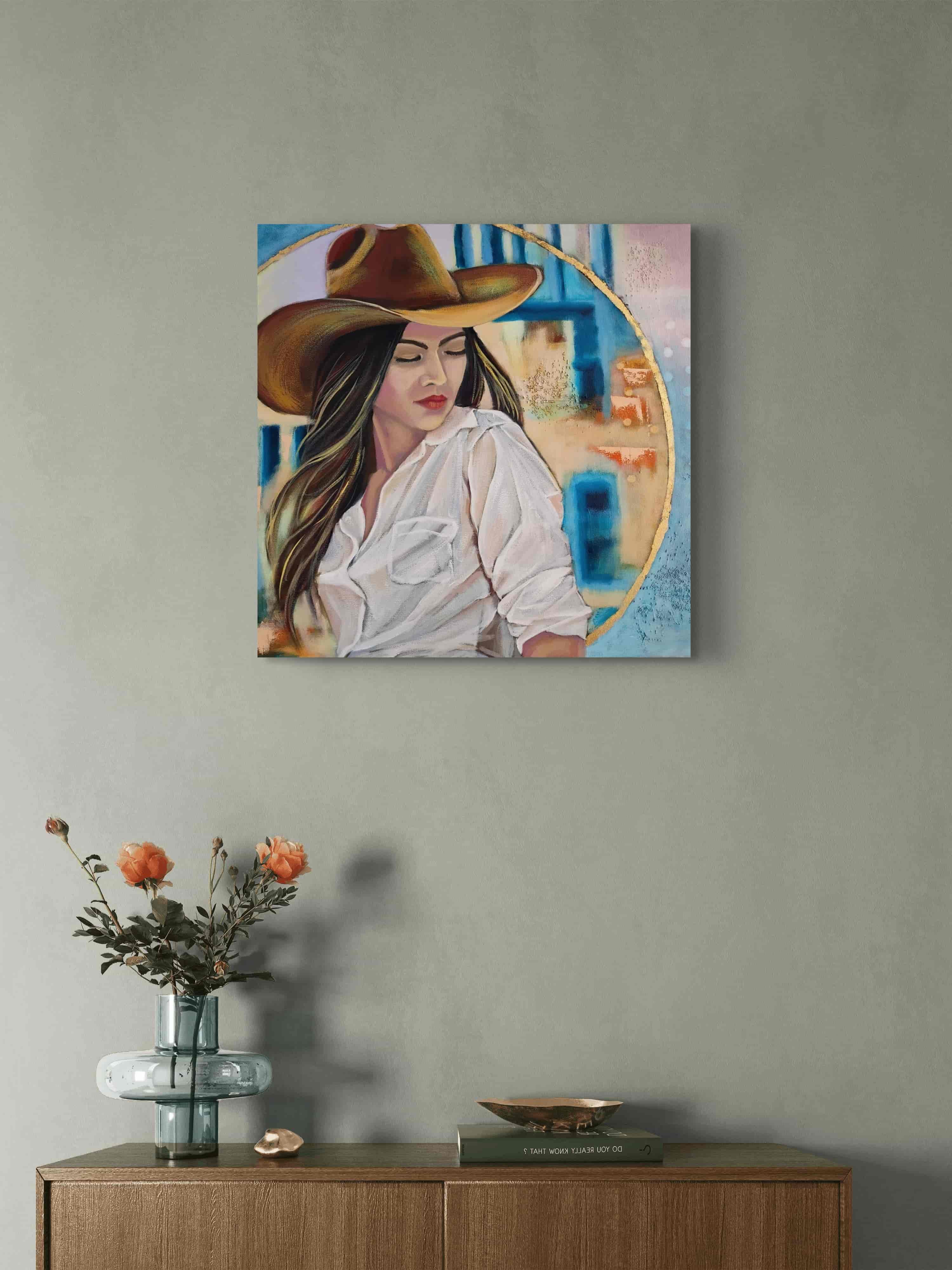 Mixed Media painting of a woman wearing a cowboy hat on a wall above a wooden side table with a vase and decorative items.