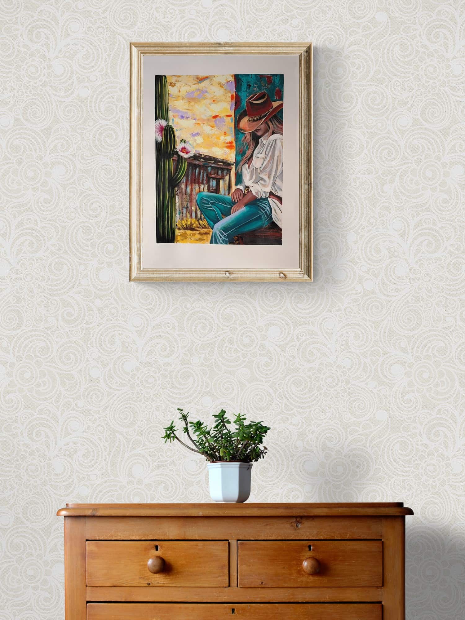 Framed artwork on a wall above a wooden dresser with a plant.