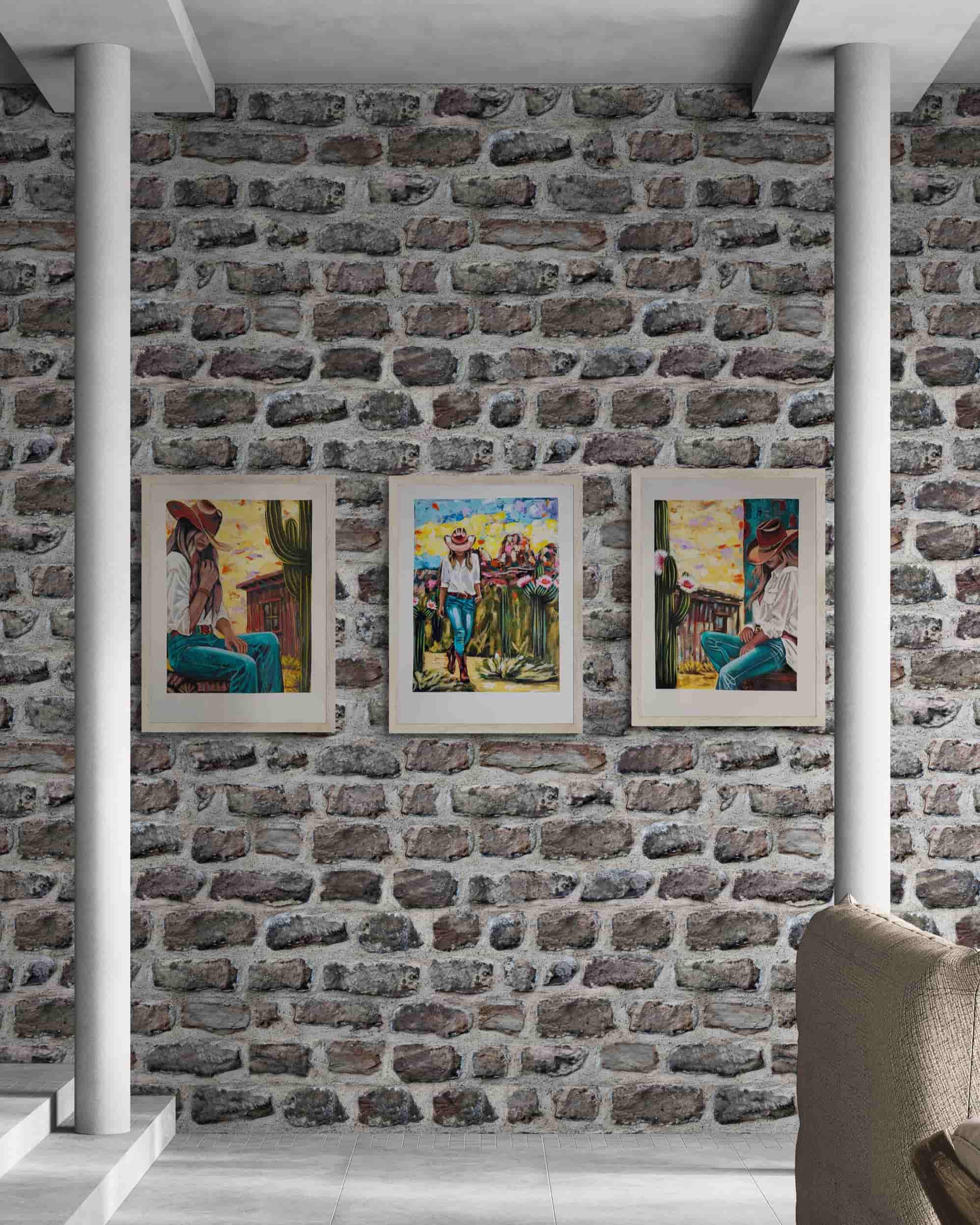 Three framed artworks on a brick wall with white columns and a chair in the foreground.