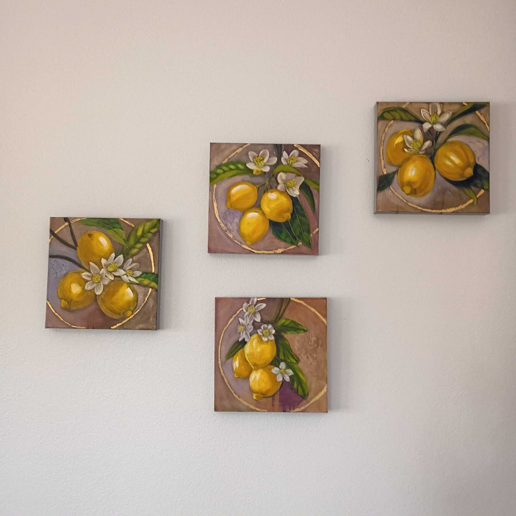 Four square paintings of lemons and flowers on a wall.