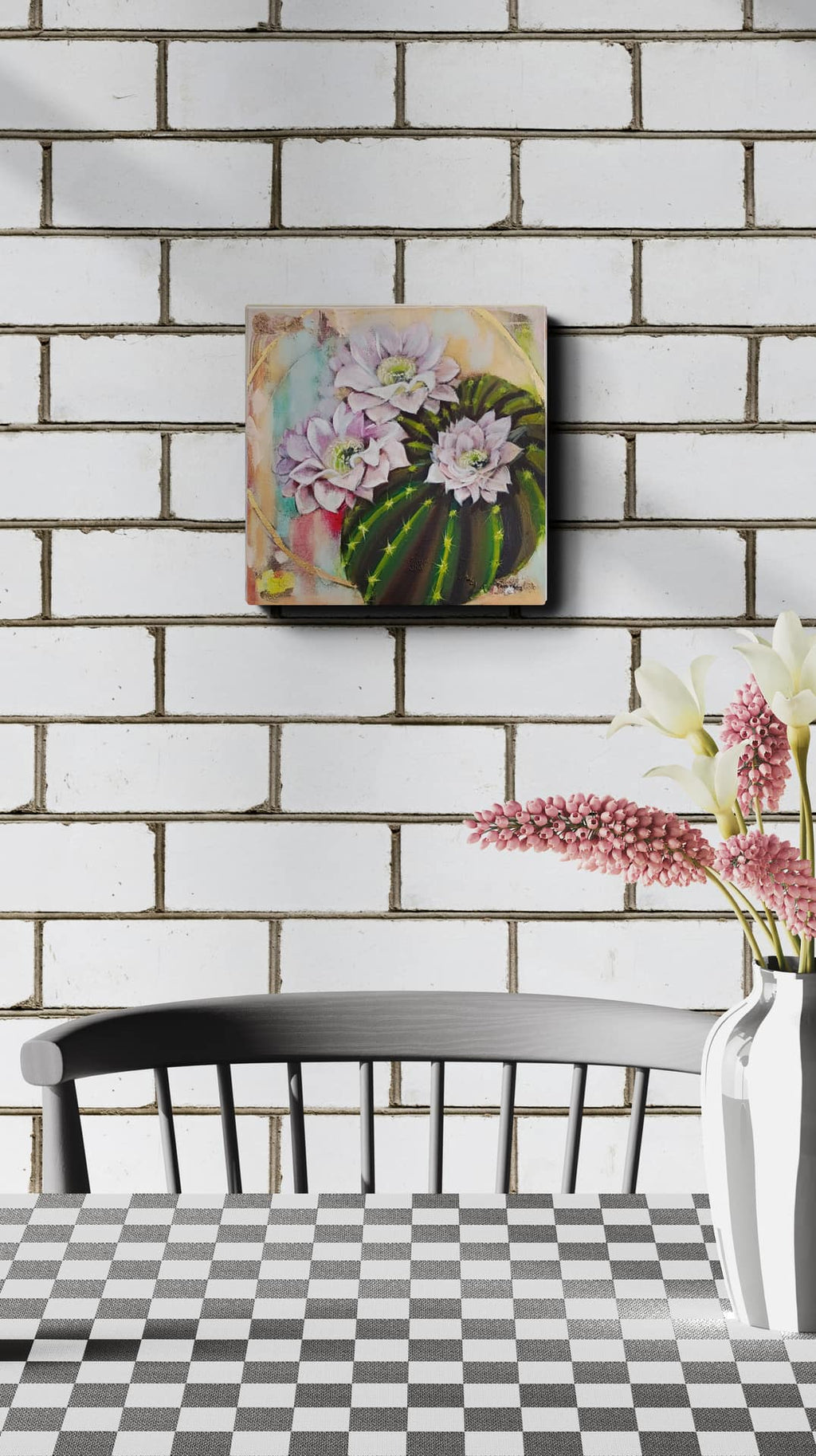 Decorative wall art with flowers on a white brick wall above a black chair and checkered table.
